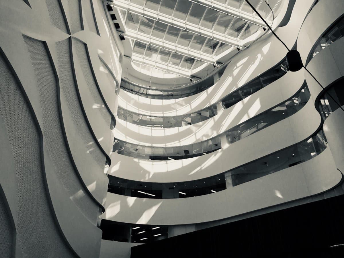 Looking up through a curved hospital atrium to the glazed roof above, in black and white.