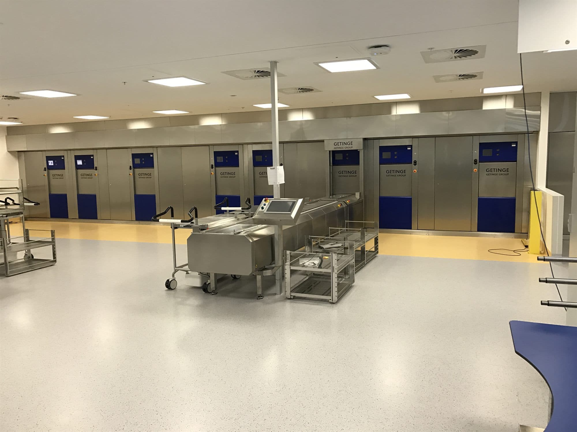 A row of stainless steel sterilisers with loading carts in a clean sterile services department.
